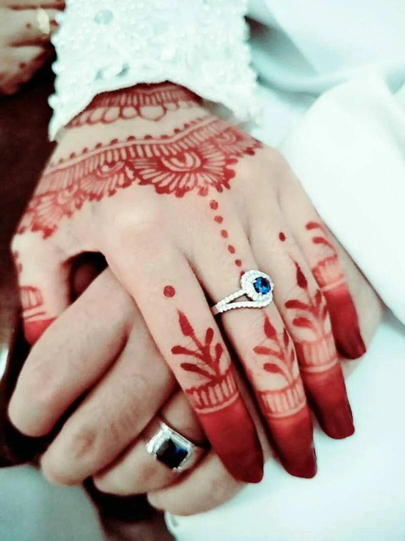 Close-up of henna-decorated hands wearing a blue-stone ring